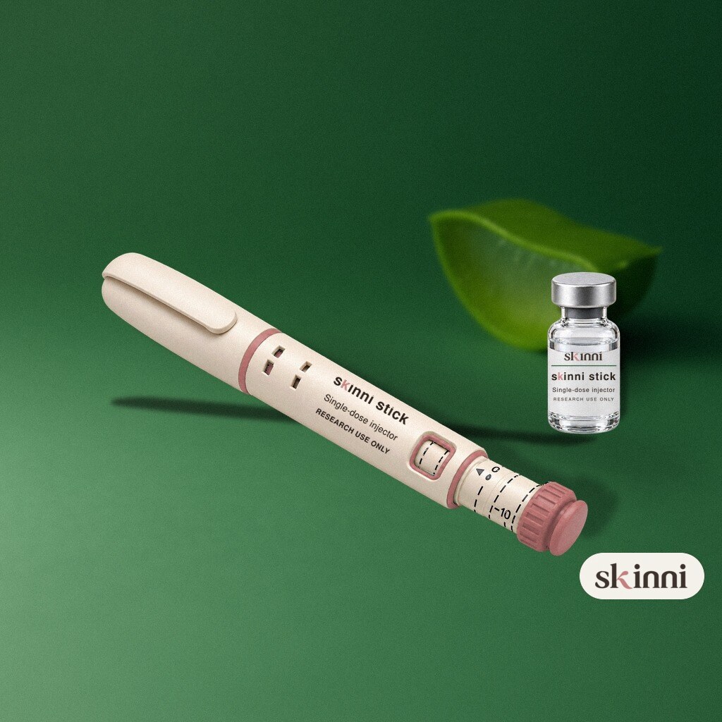 A clear GHK-Cu research vial on a coloured plaster ledge, with botanicals beside it